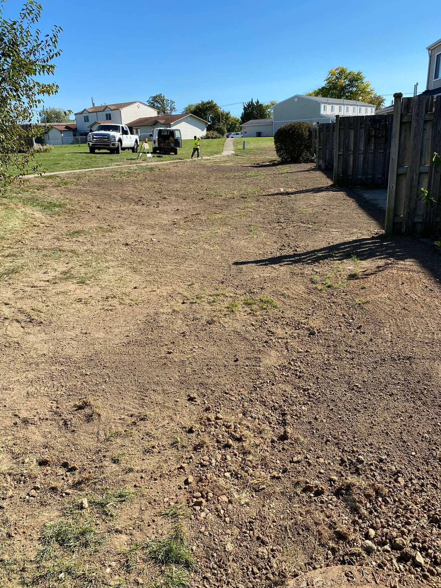 A dirt field with a fence and a house in the background.