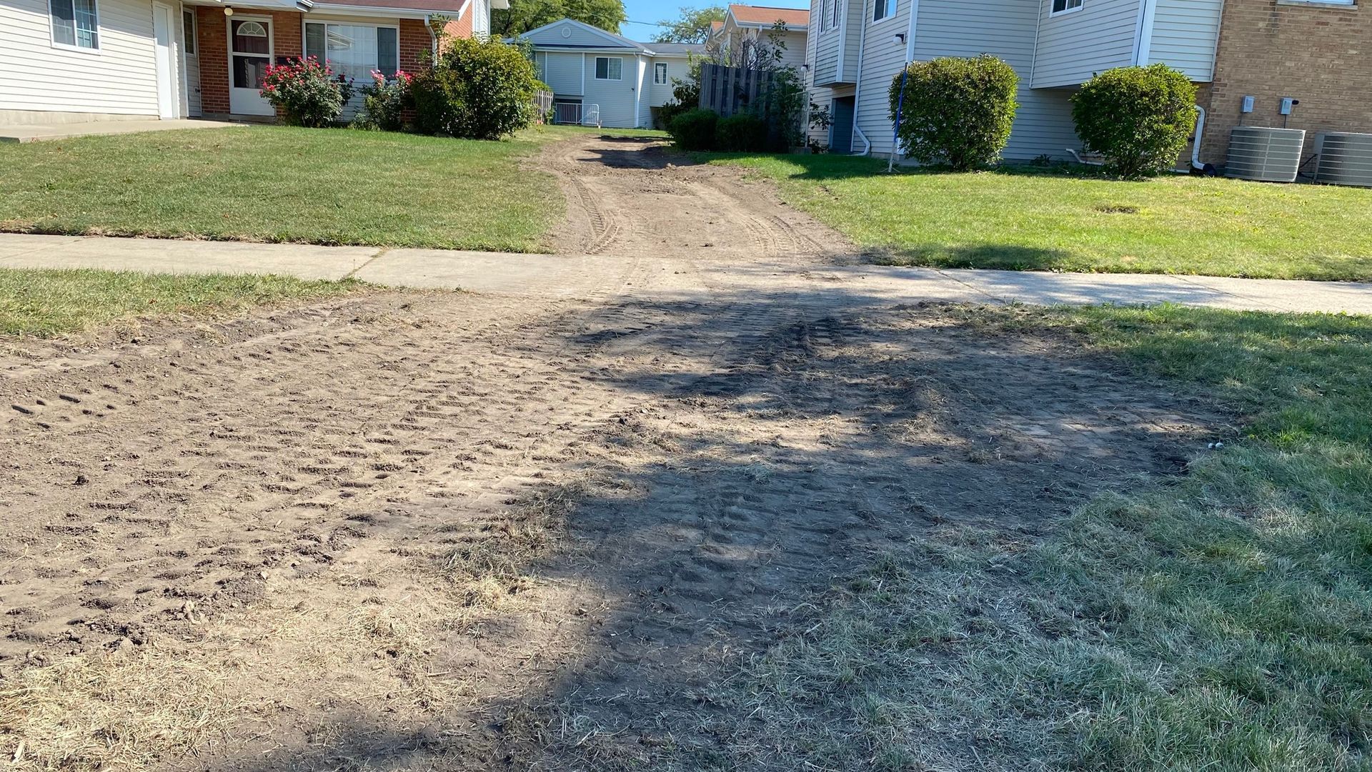 A dirt road leading to a house in a residential neighborhood.