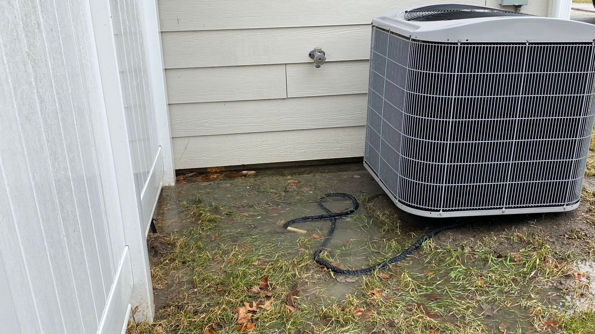 An air conditioner is sitting on the ground next to a white fence.
