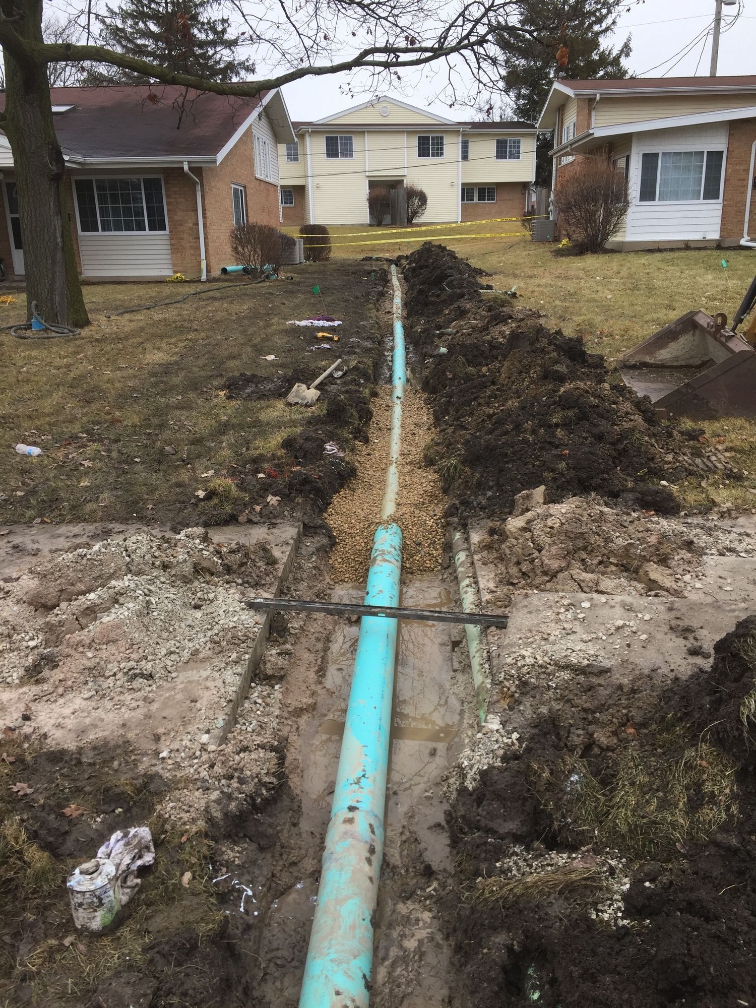 A green pipe is laying in the dirt in front of a house.