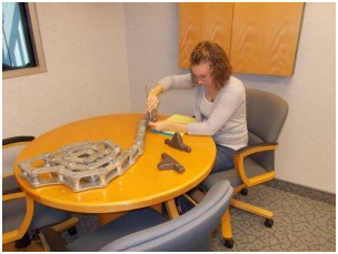 A woman sits at a table with a piece of metal on it – USA - Regal Construction Inc.