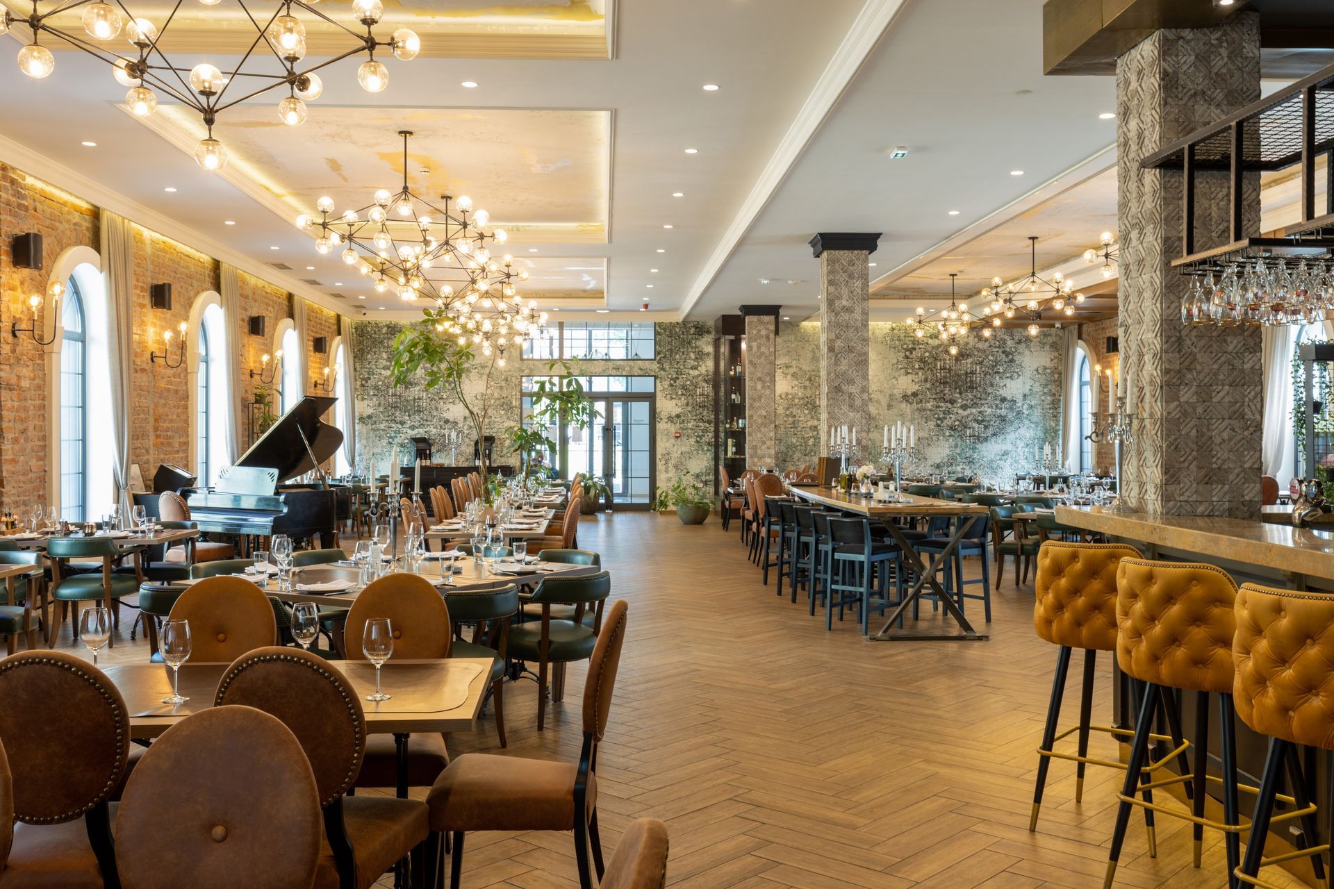 Elegant restaurant interior with gold accents, rows of tables, and tufted bar stools along a mirrored wall
