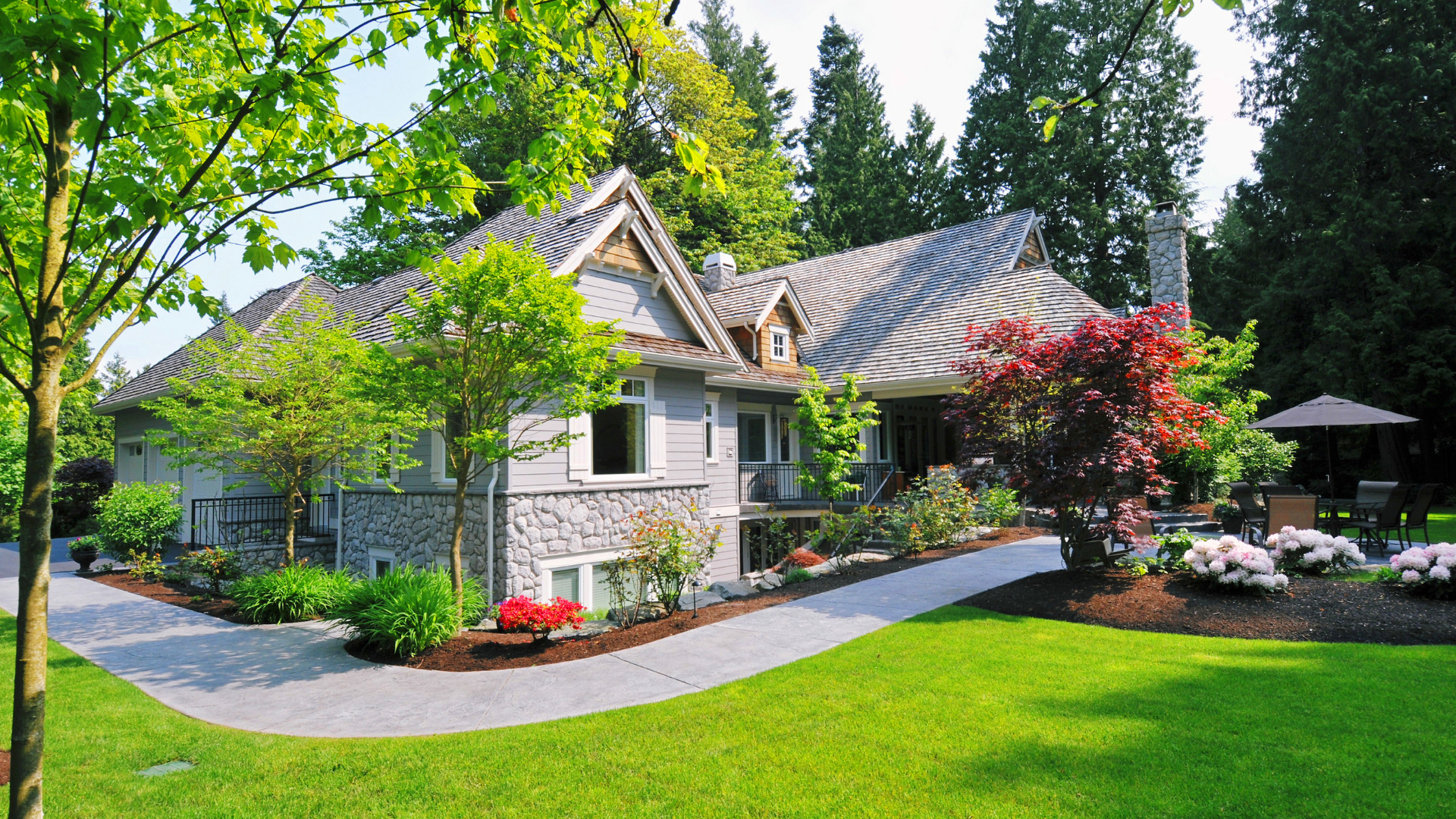 House with gray siding and stone accents surrounded by lush green lawn and landscaping.