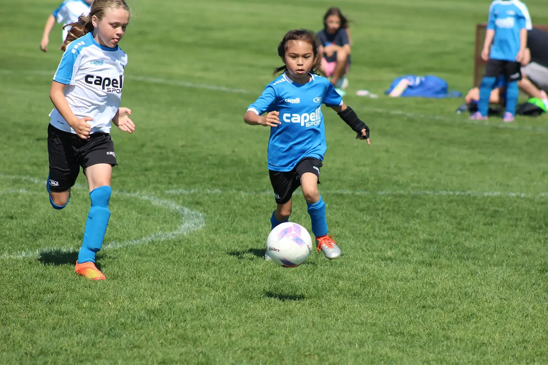 two young girls chasing a soccer ball on a field