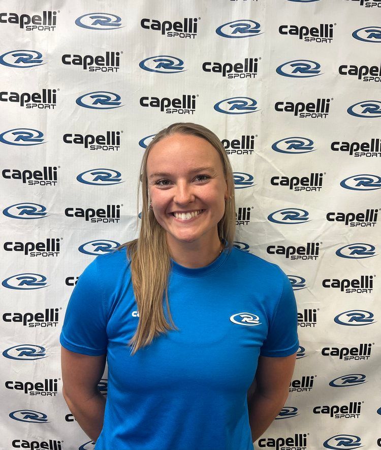 A woman in a blue shirt is standing in front of a wall with capelli written on it.