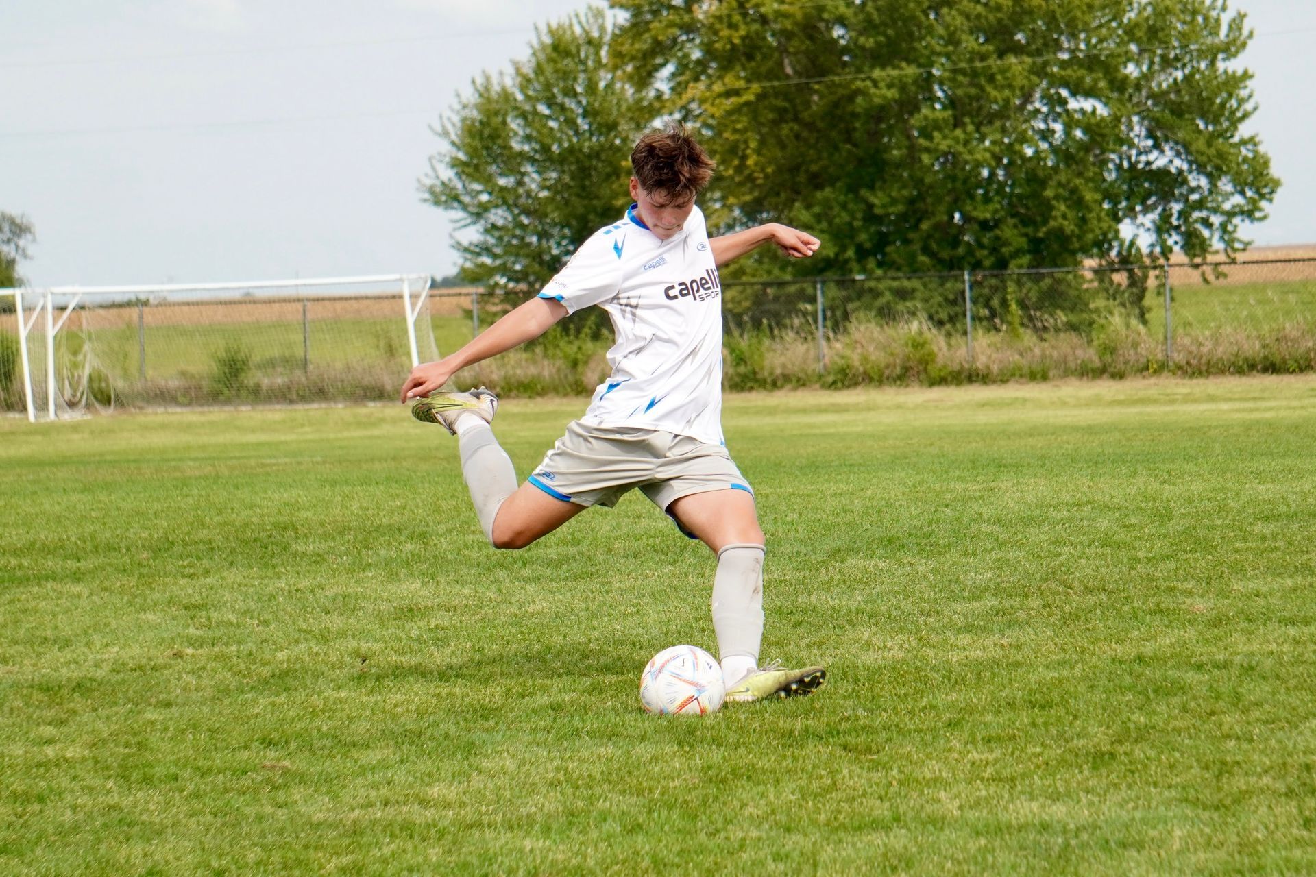 boy soccer player kicking ball in a white uniform