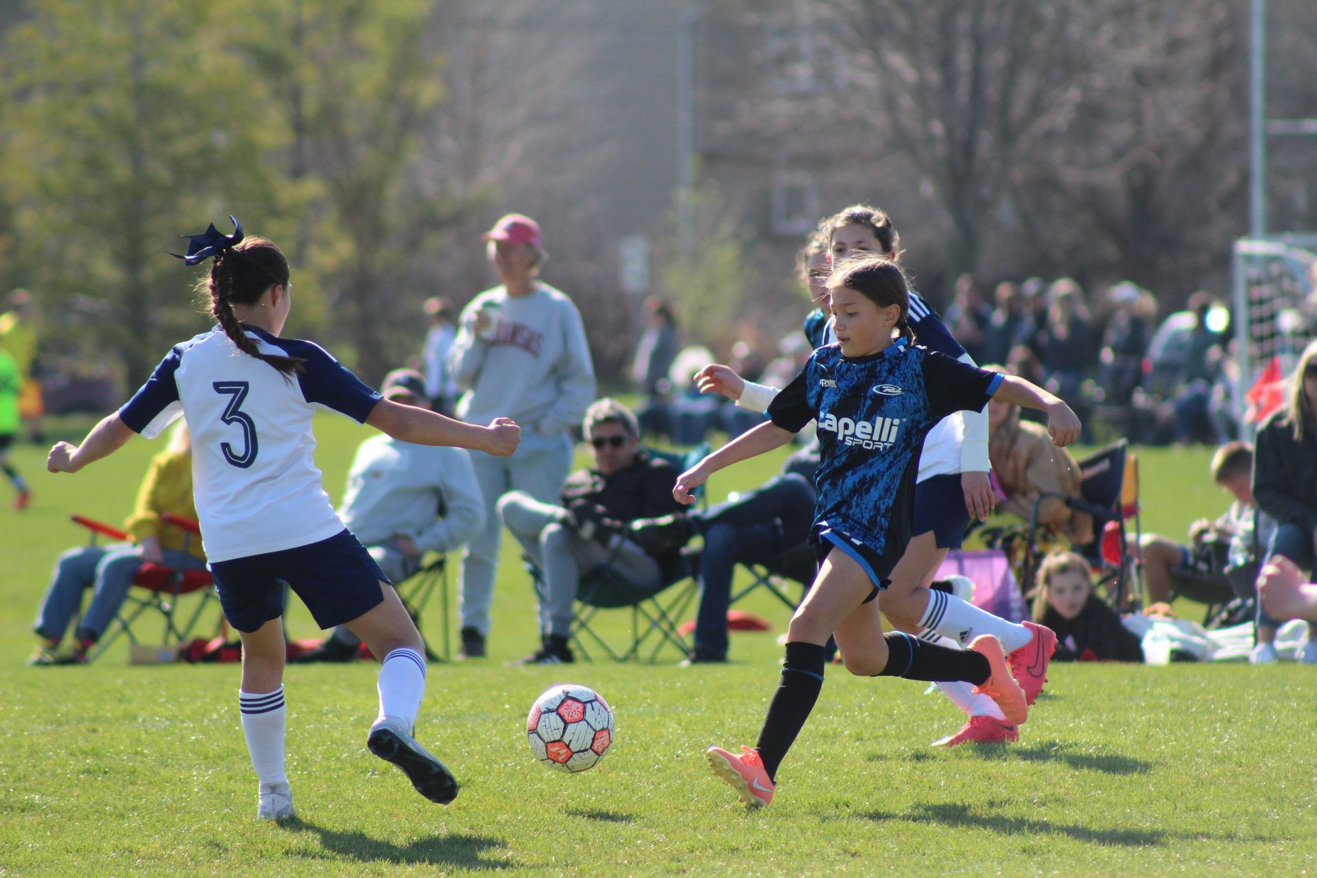 youth soccer girls kicking a ball during a game. One team in white the other blue