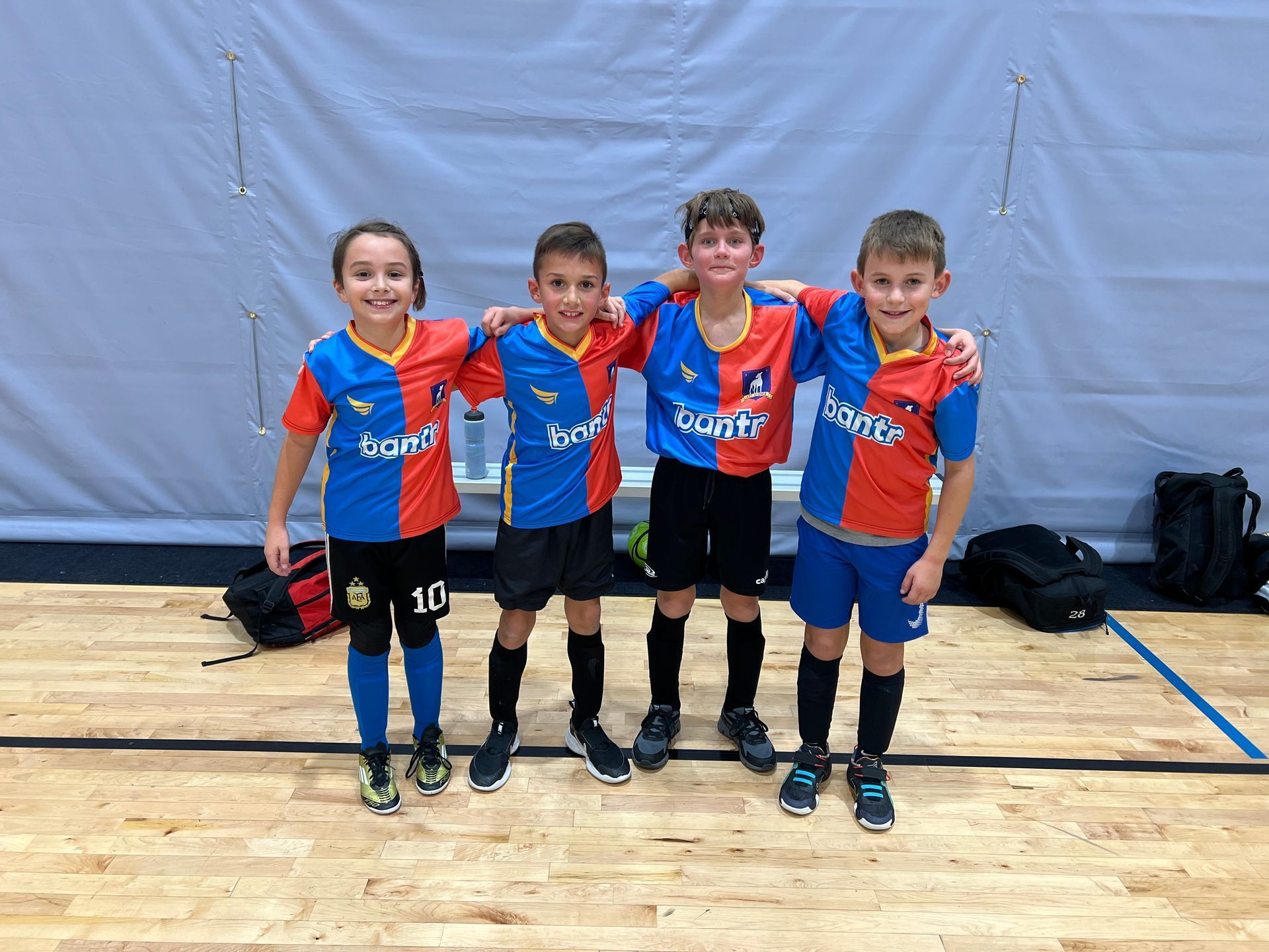 A group of young futsal boys are posing for a picture on a wooden floor.
