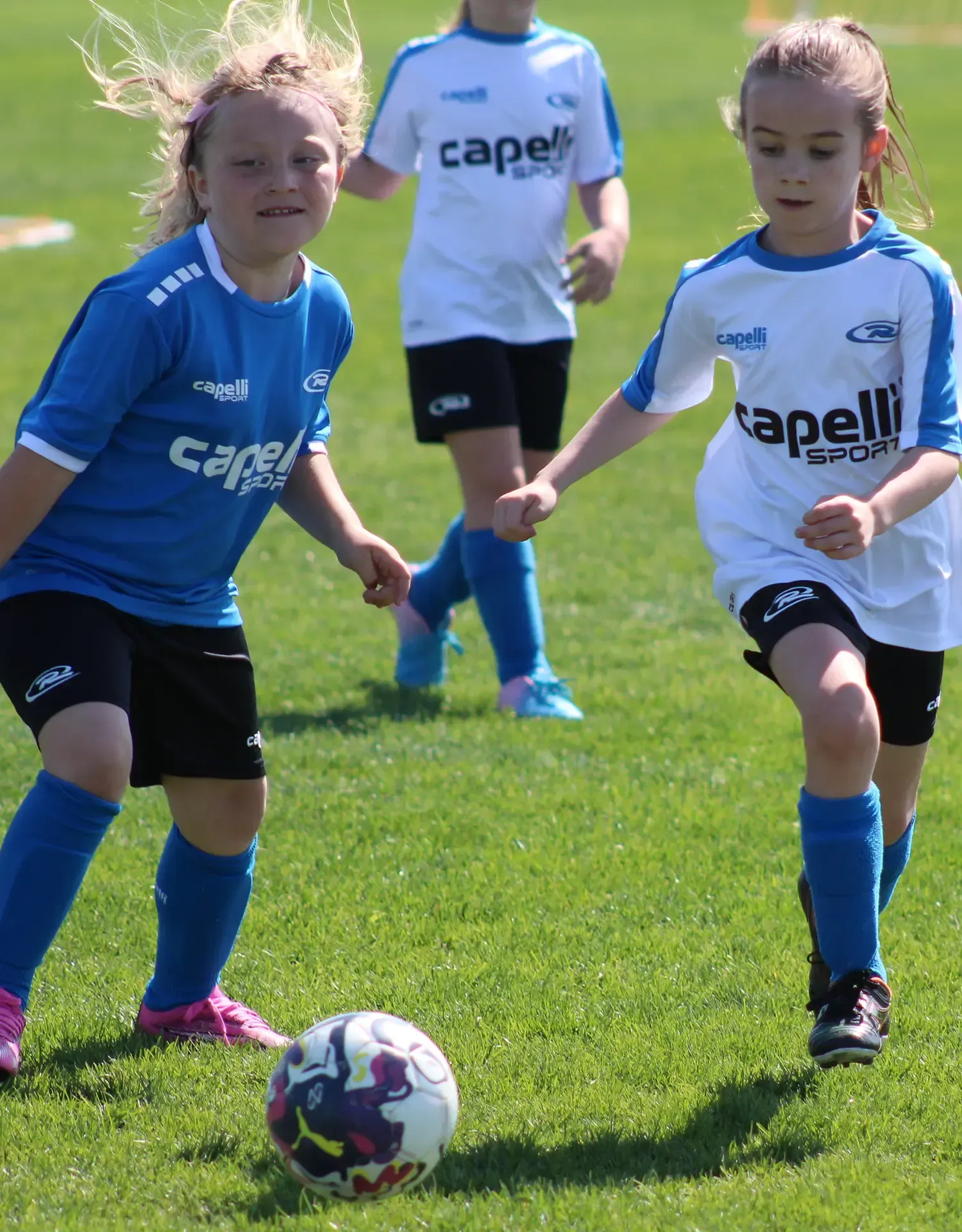 Two girls are playing soccer and one has the word capell on her shirt