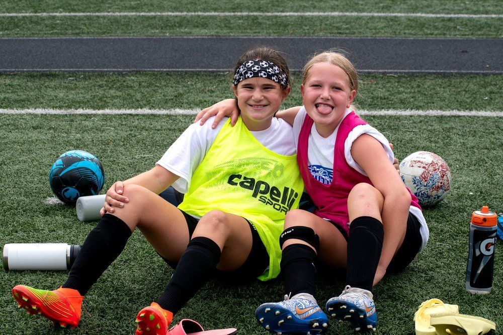 two girl soccer players smiling at camera sitting on the sidelines