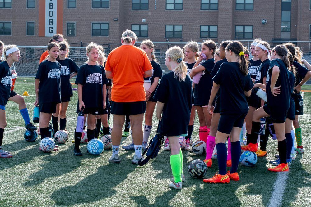 A group of young girls are standing on a field with soccer balls.