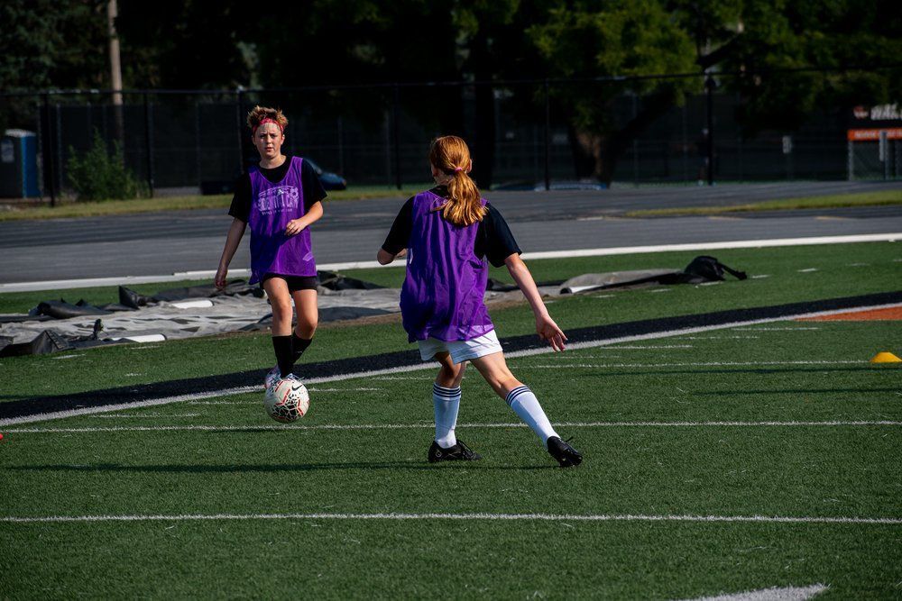 Two young girls are playing soccer on a field.
