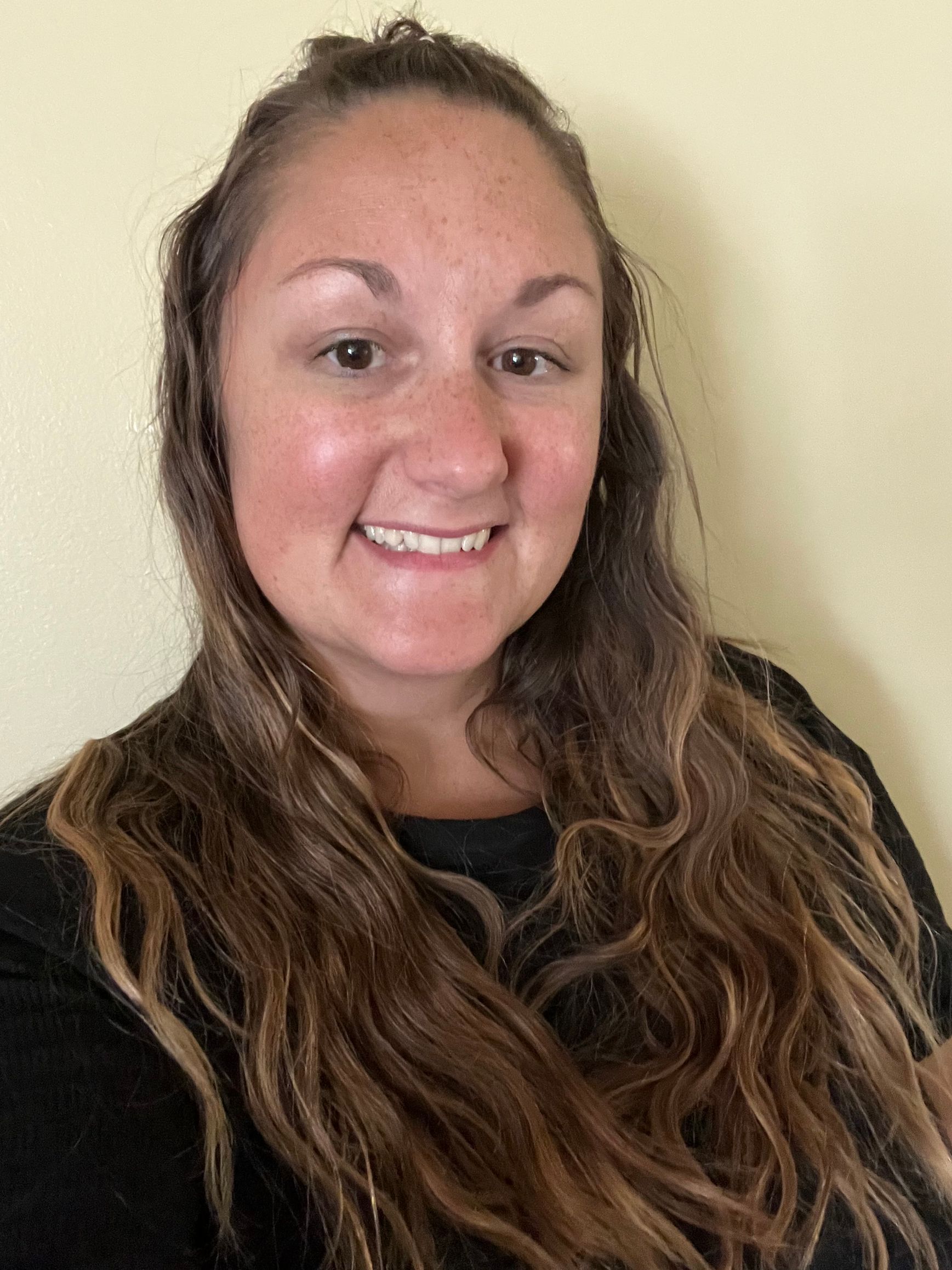 A woman with long brown hair is smiling for the camera.