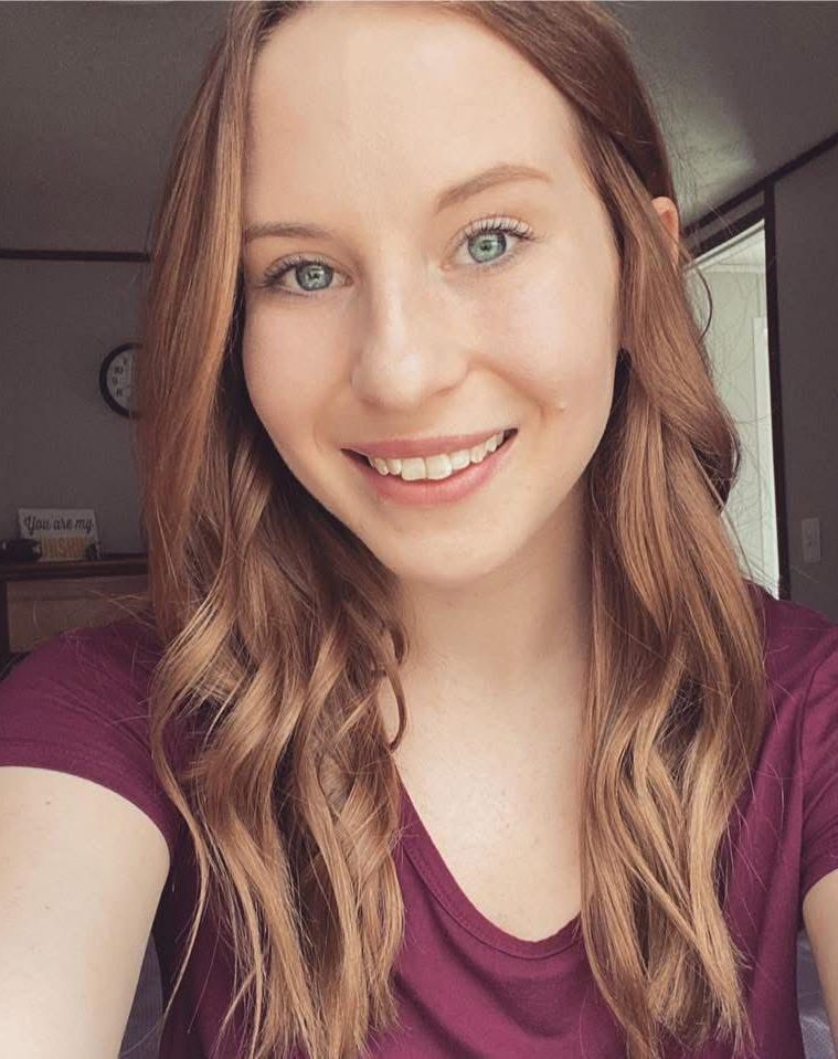 A woman in a purple shirt is smiling and taking a selfie