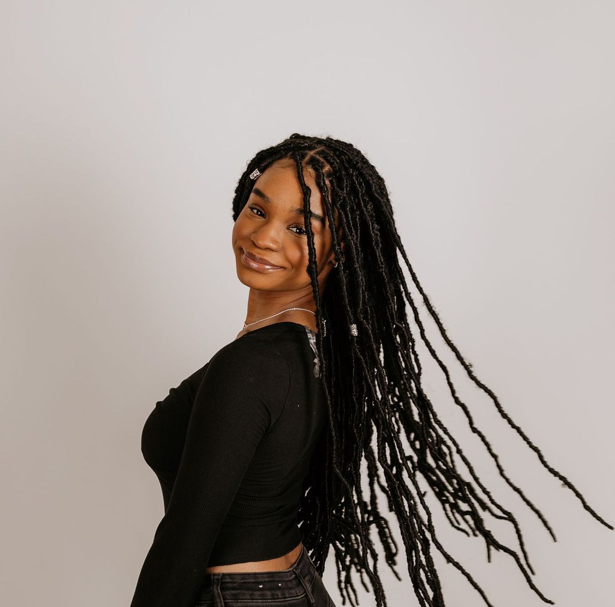 A woman with dreadlocks is wearing a black top and jeans.