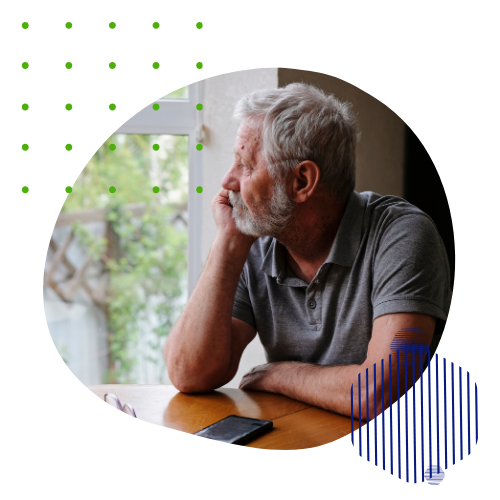 An older man is sitting at a table looking out a window.
