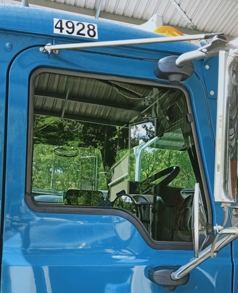 Blue truck cab with side window, mirror, and steering wheel visible inside.