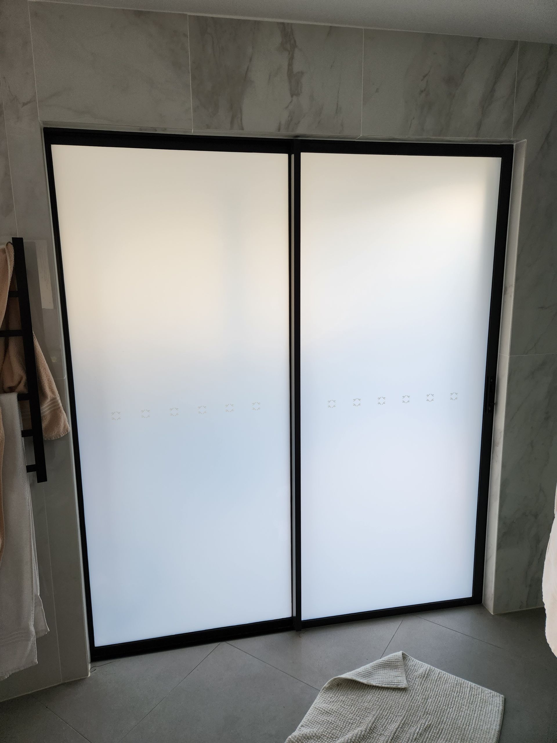 Frosted glass shower doors with black frames in a bathroom with gray walls and floor.