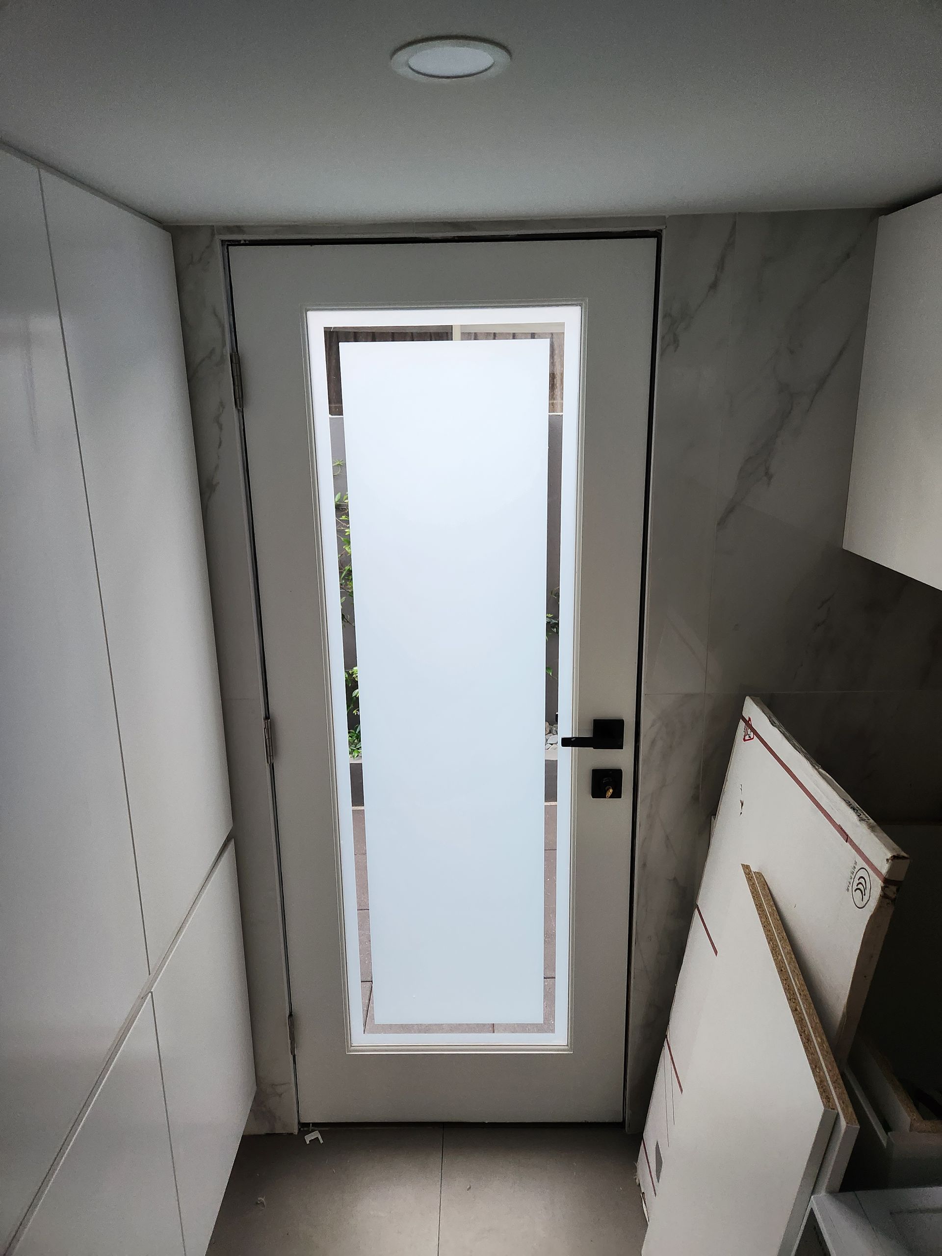 White door with frosted glass panel in a narrow hallway with built-in cabinetry and unfinished panels.
