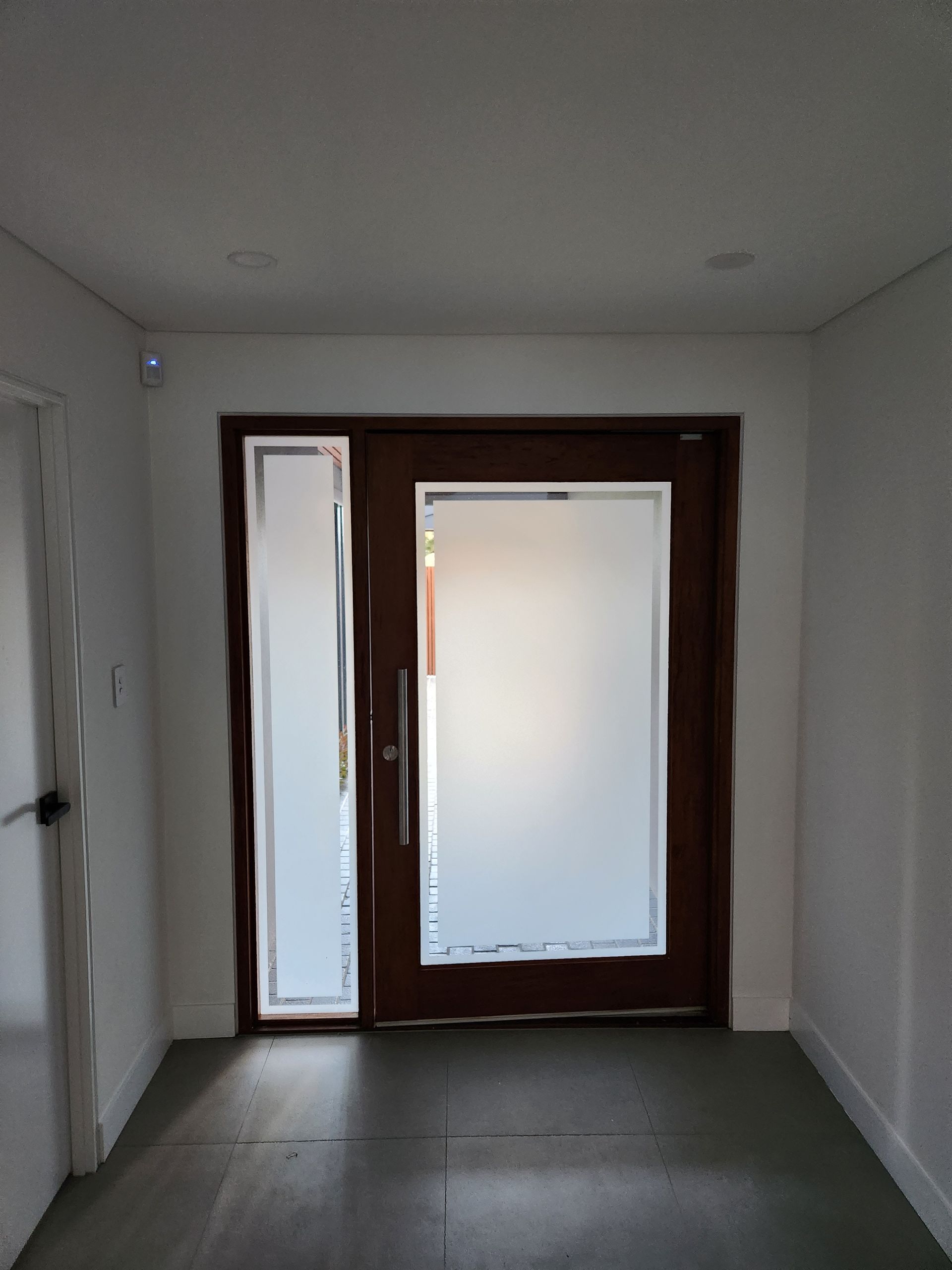 Wooden front door with frosted glass and sidelight. Interior view of a hallway.