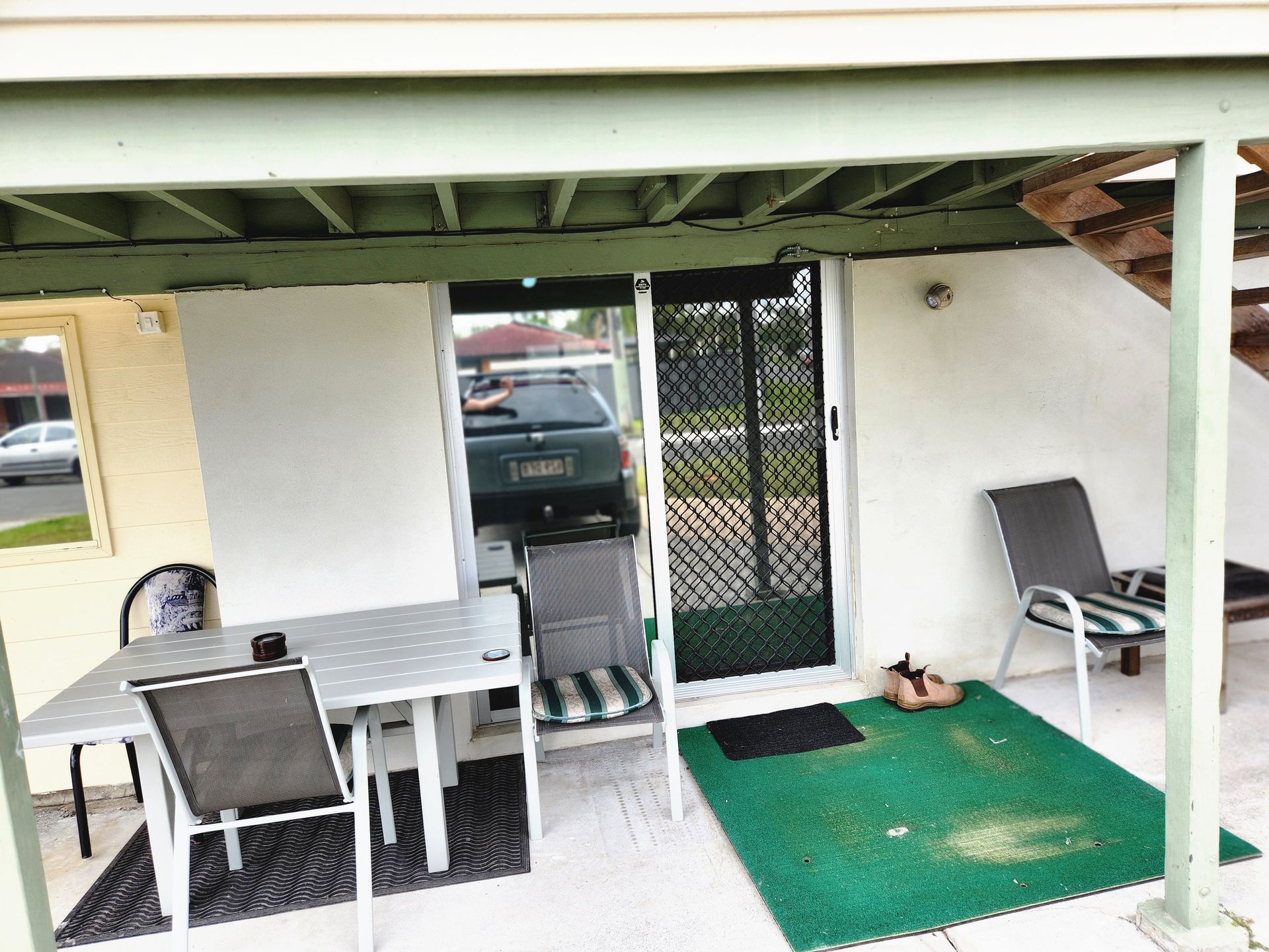 Patio with table, chairs, sliding door, and green carpet under a covered area. A car is visible.