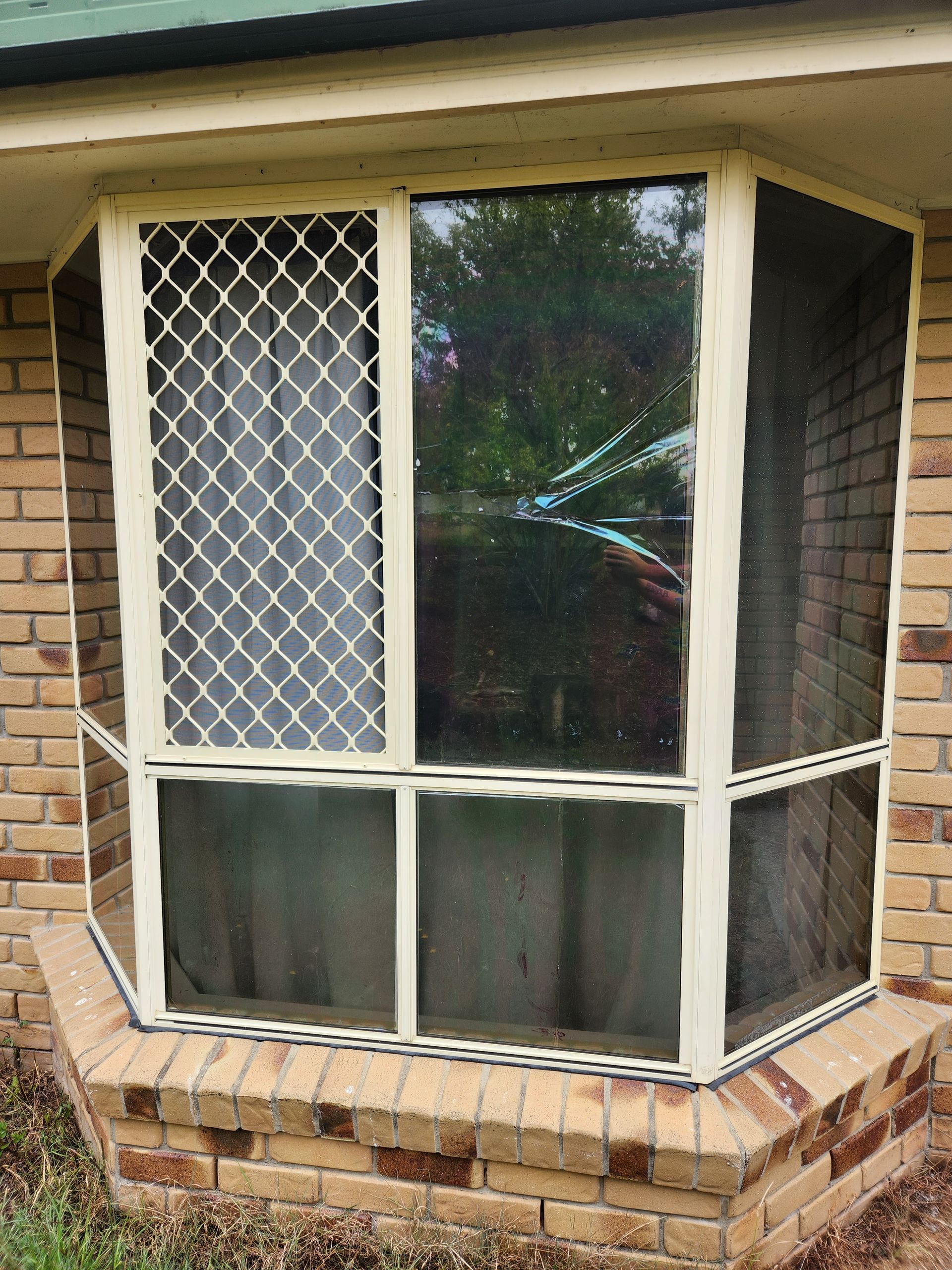 Bay window with beige frames, security screen, and brick facade.