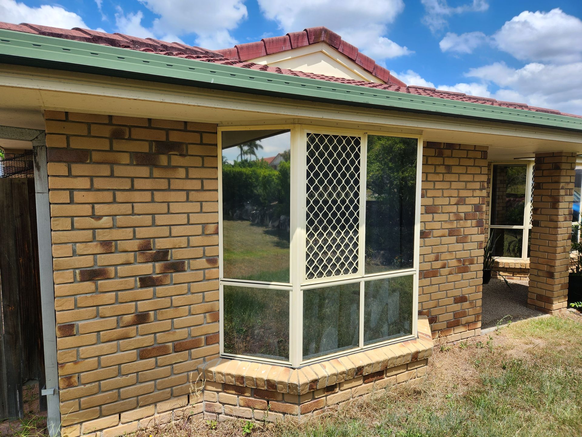 Brick house exterior with a large window, security screen, and a red tiled roof.