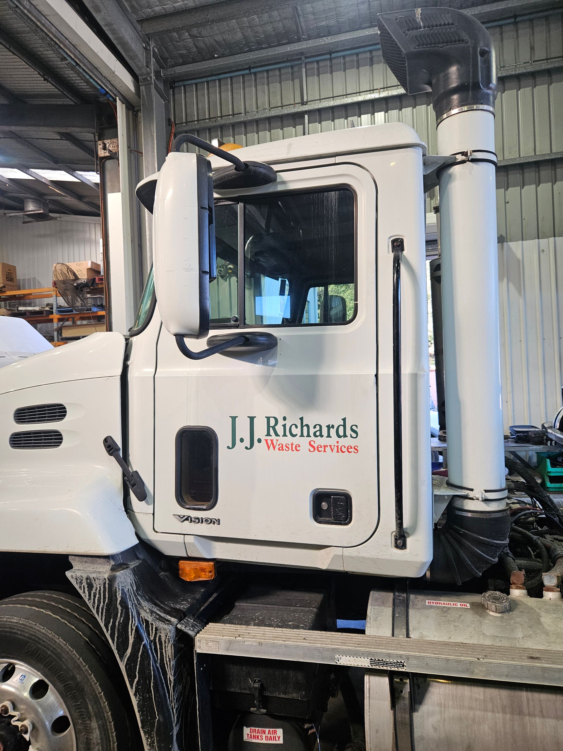 White J.J. Richards waste services truck cab with side mirror and exhaust pipe.