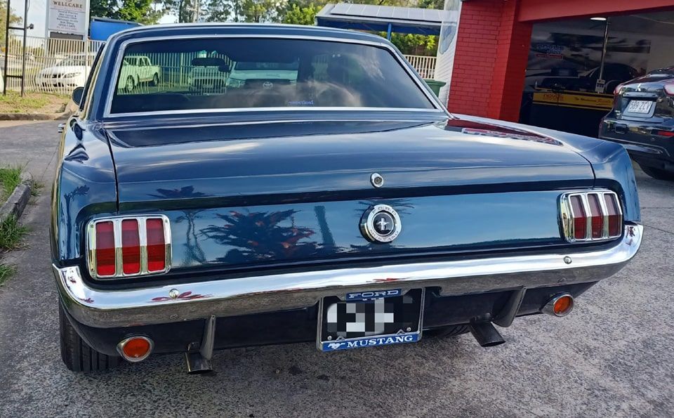 Rear view of a classic blue Ford Mustang parked outside a building.