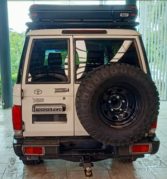 White Toyota Land Cruiser with spare tire, roof rack, and a trailer hitch.
