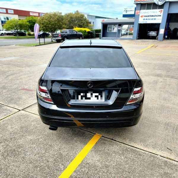 Black Mercedes sedan parked outside a tire shop, rear view.