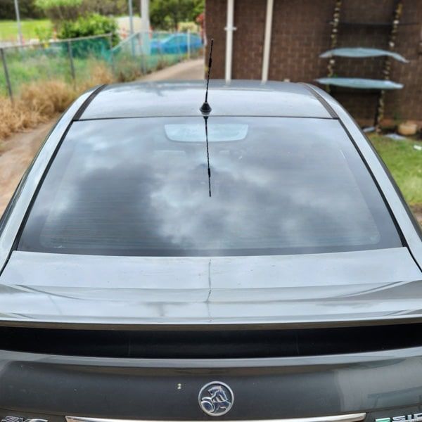 Rear view of a dark gray car with a cracked rear window and a spoiler.