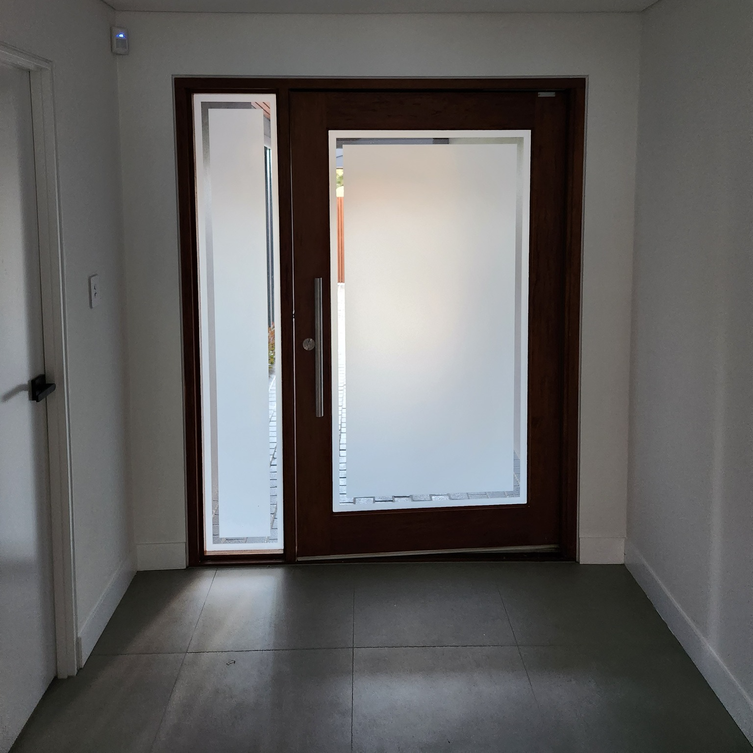 Brown wooden door with frosted glass and sidelight in a white hallway.