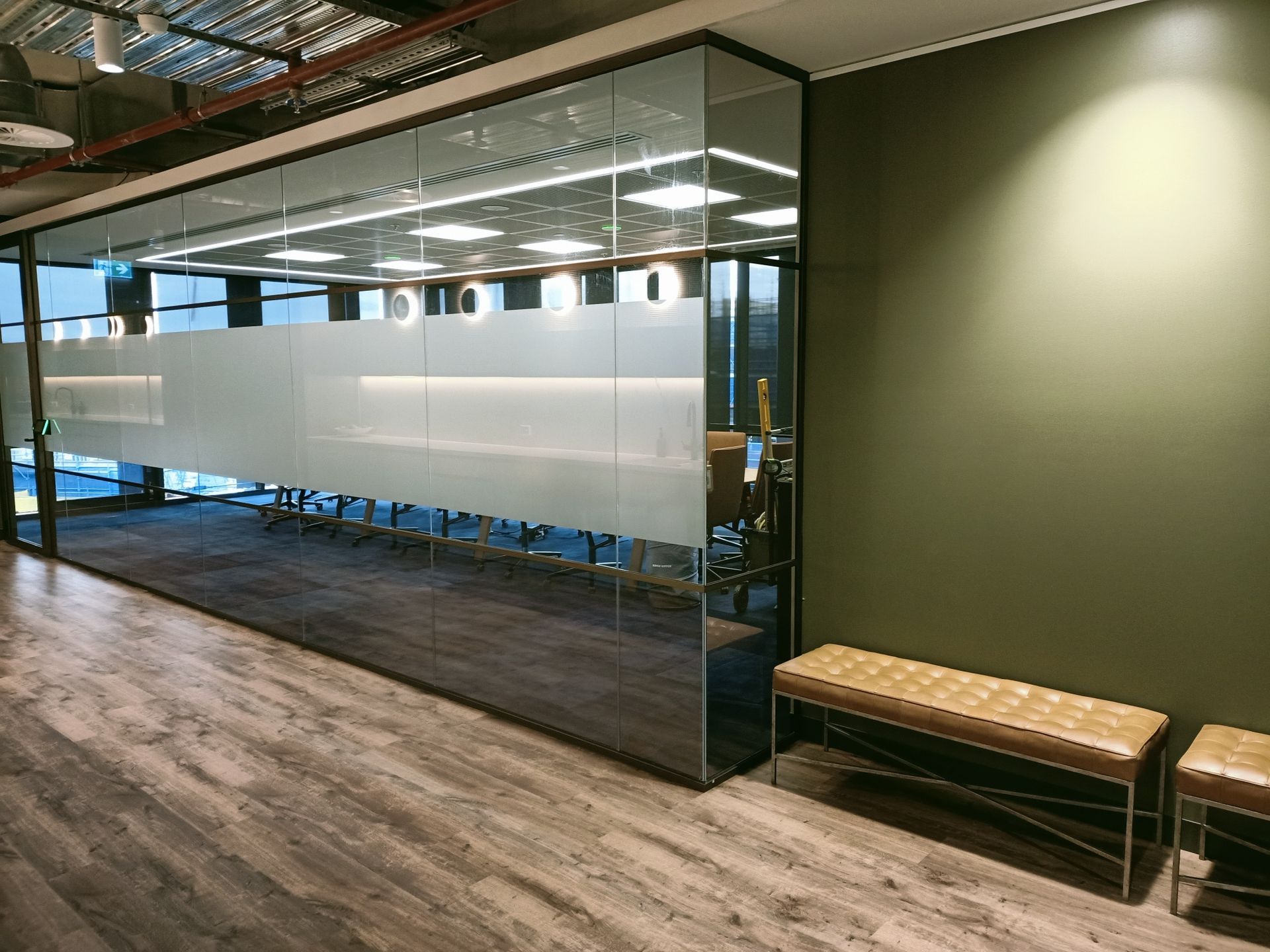 Conference room with glass walls, frosted band, olive green wall, and brown bench.