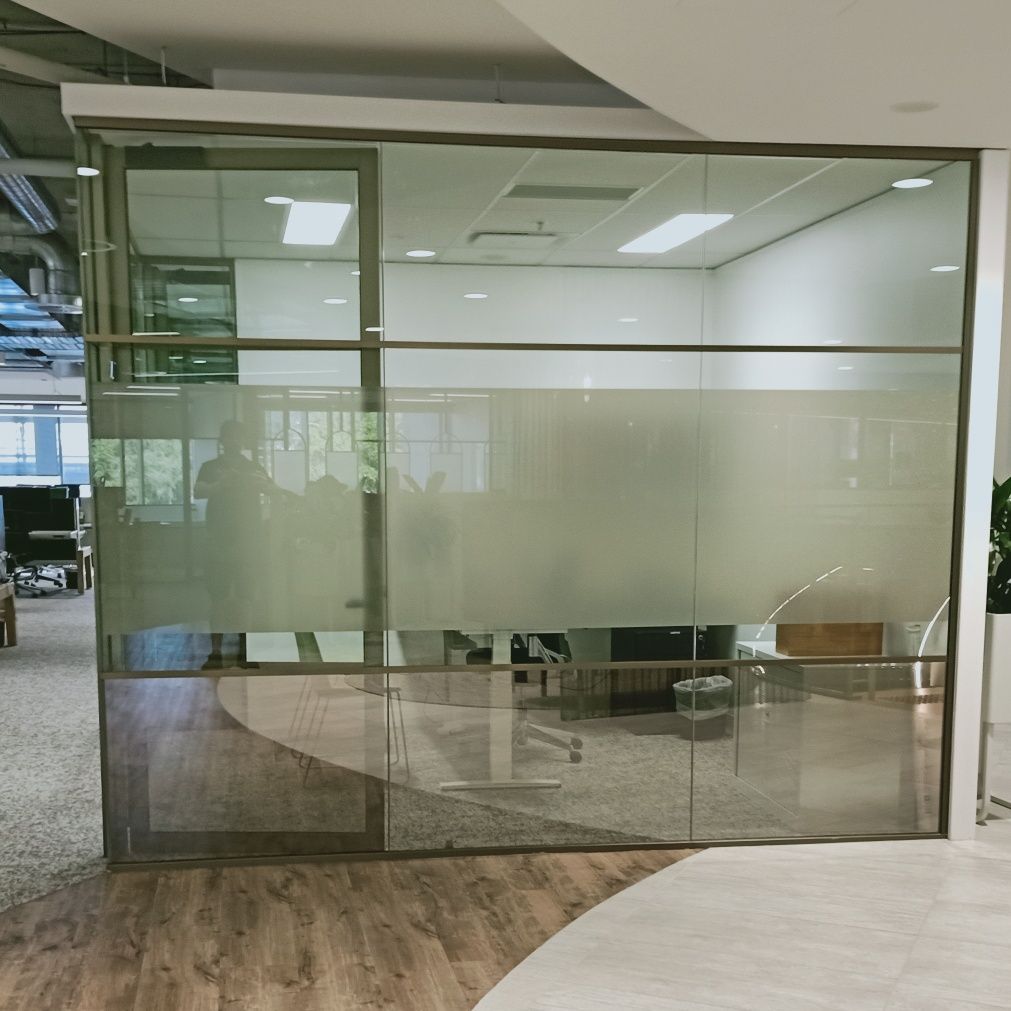 Glass-walled office with frosted privacy band, featuring a door, and a glimpse of interior furnishings.