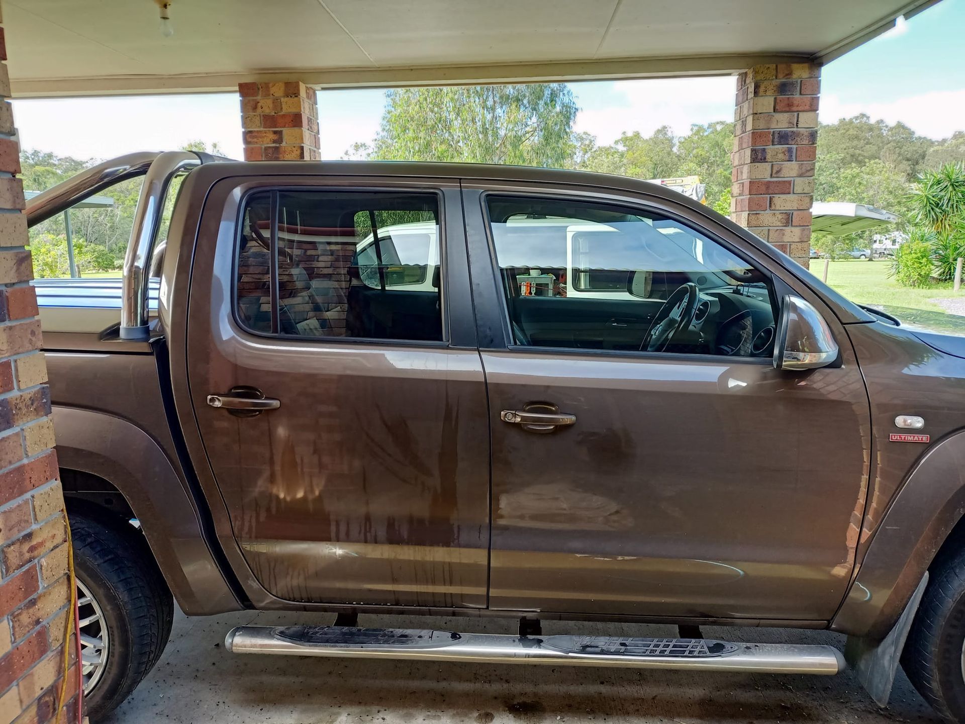 Brown pickup truck parked under a covered area, with a view of greenery in the background.