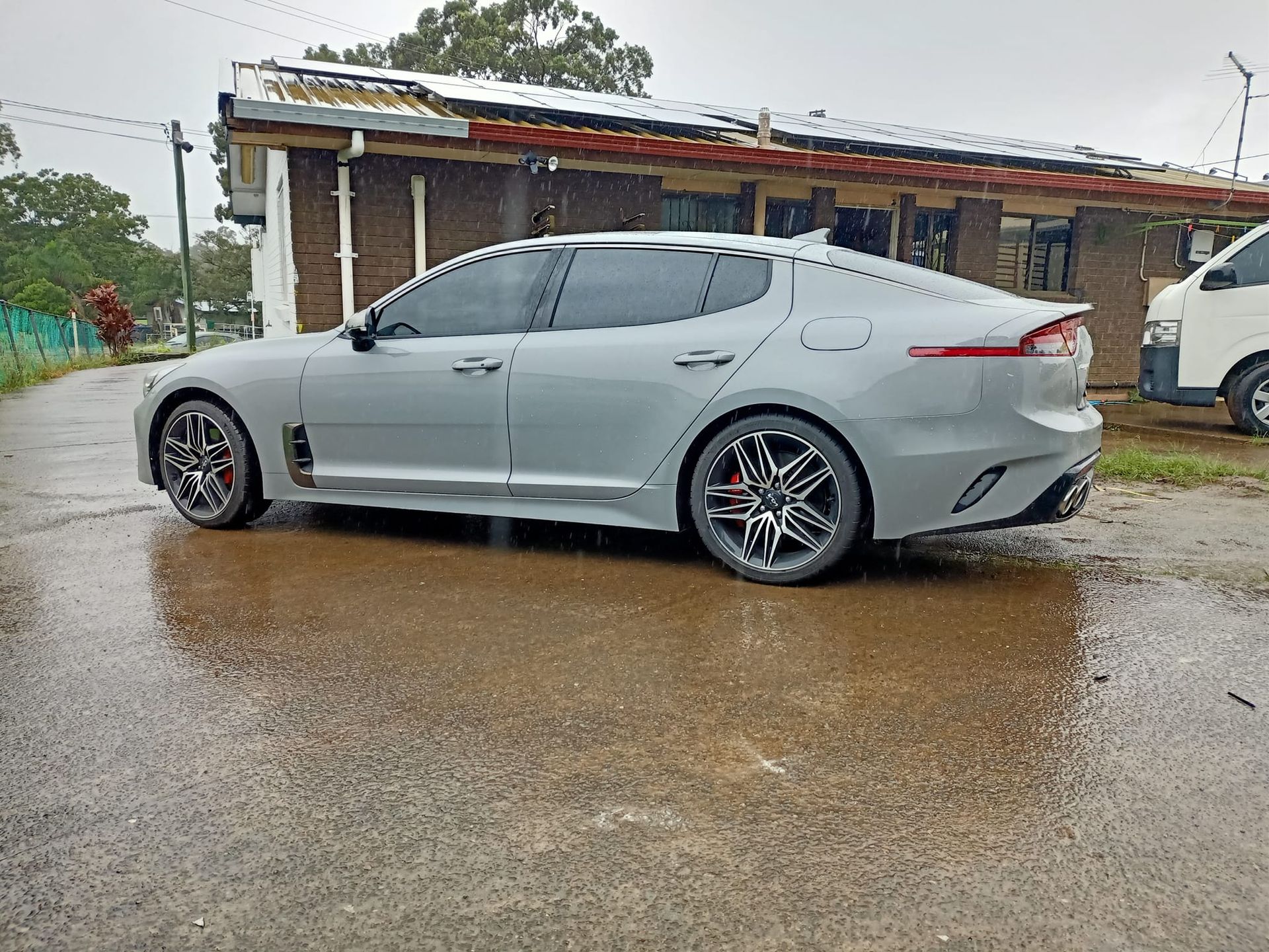 Gray Kia Stinger parked on a wet road in front of a building during rain.