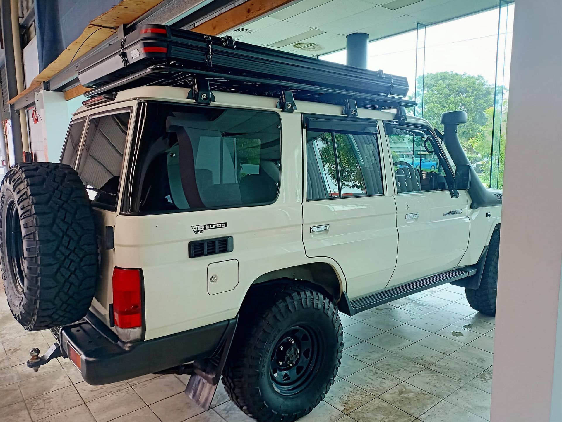 White off-road vehicle with black wheels and a roof rack, parked indoors.