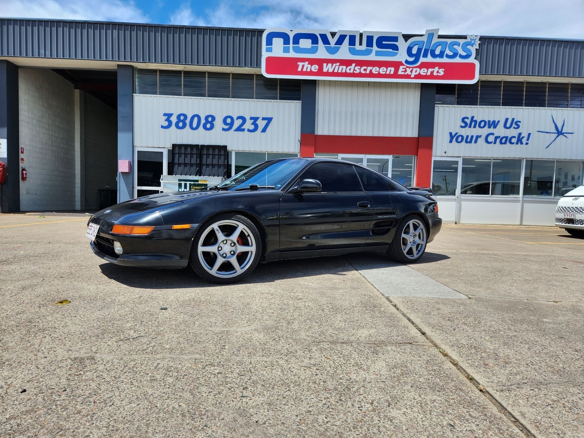 Black sports car parked outside a Novus Glass repair shop.