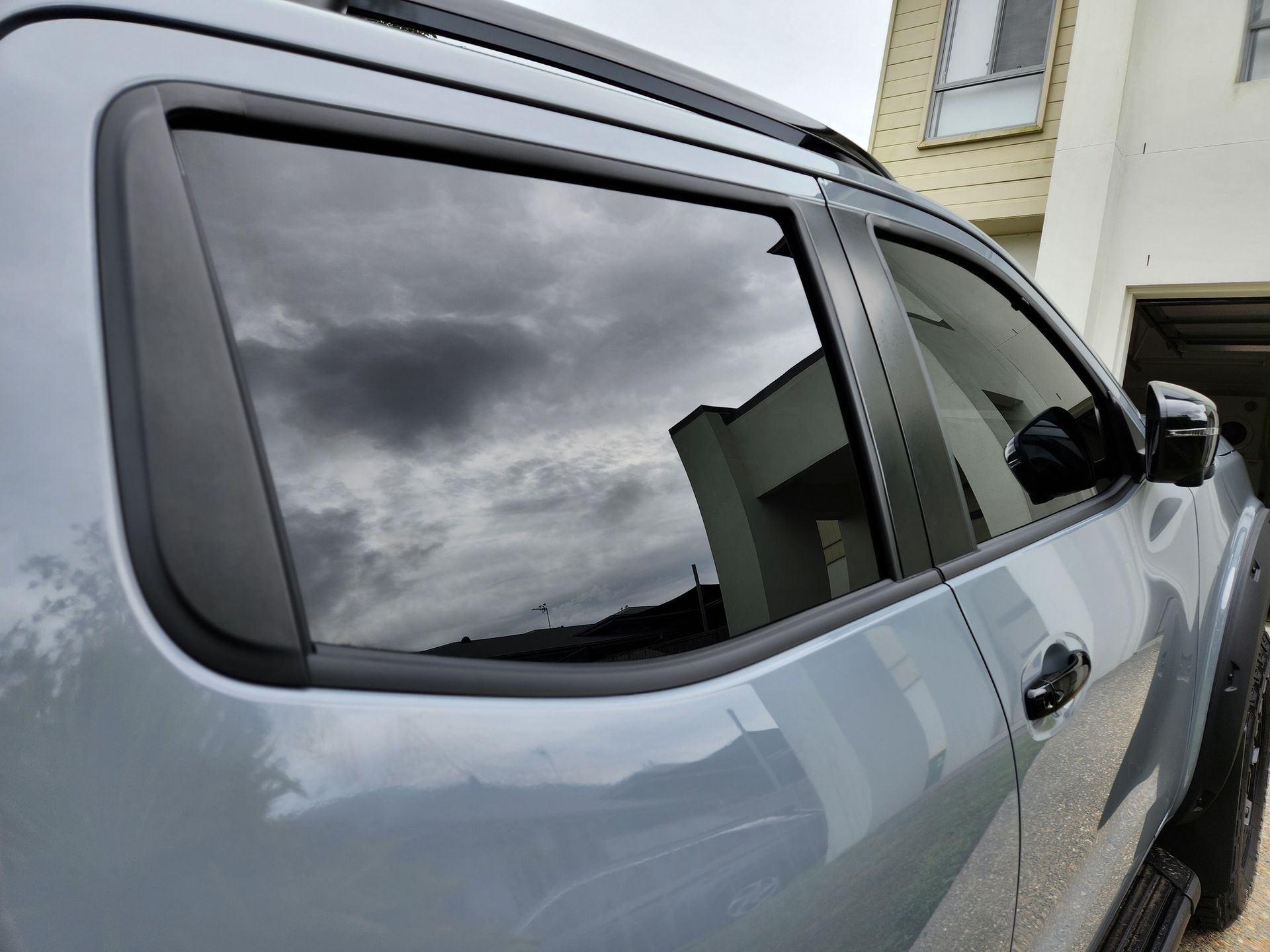 Gray truck with tinted windows reflecting cloudy sky and building.