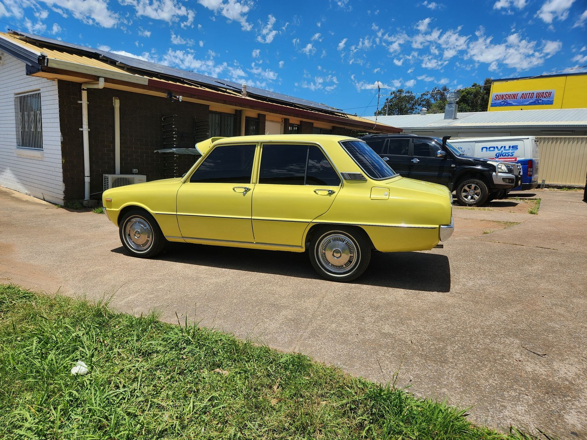 Yellow vintage car parked outside a building on a sunny day.