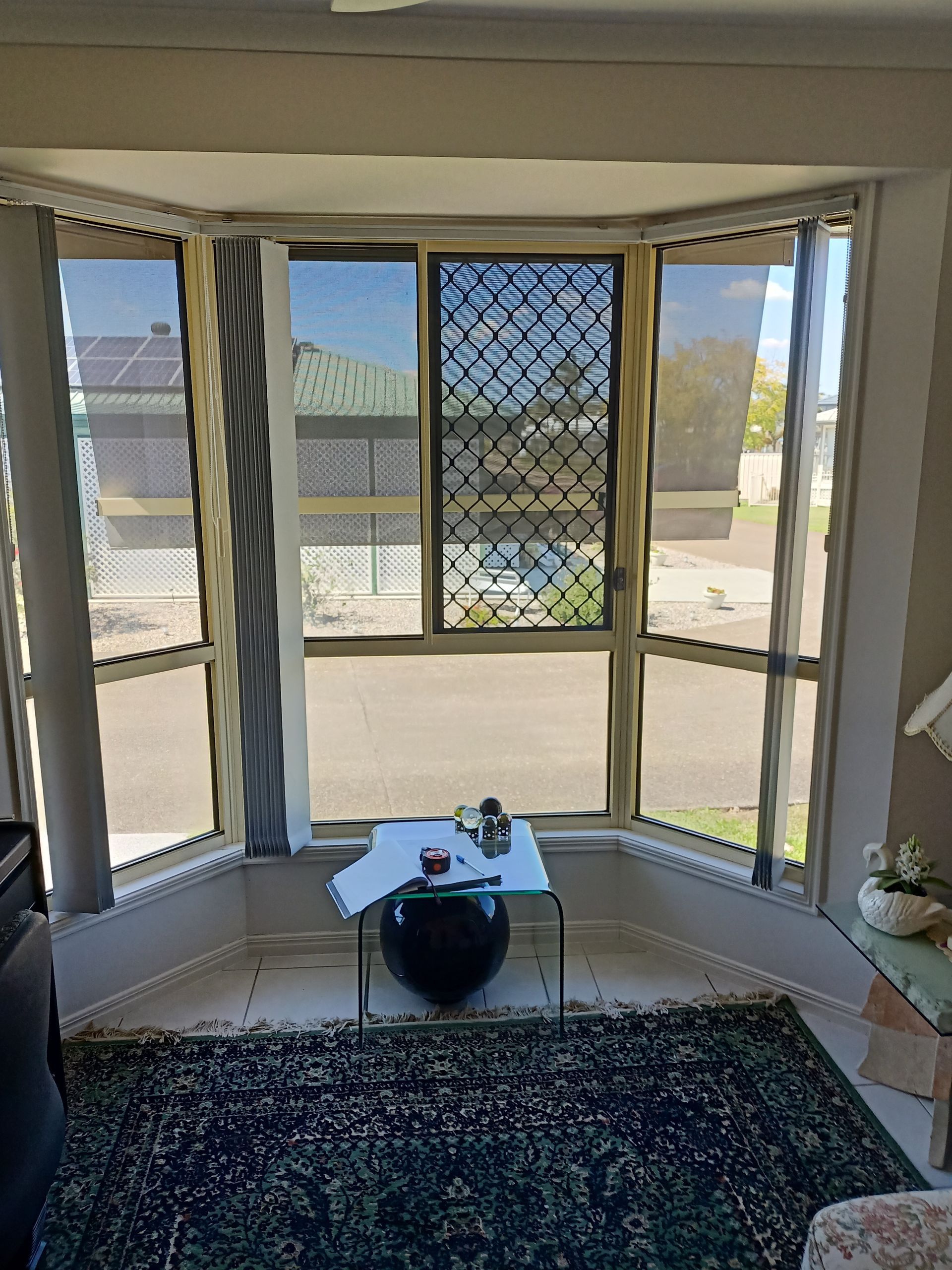 Bay window with security screens overlooking a street. A rug, table, and decorations are in front of the window.