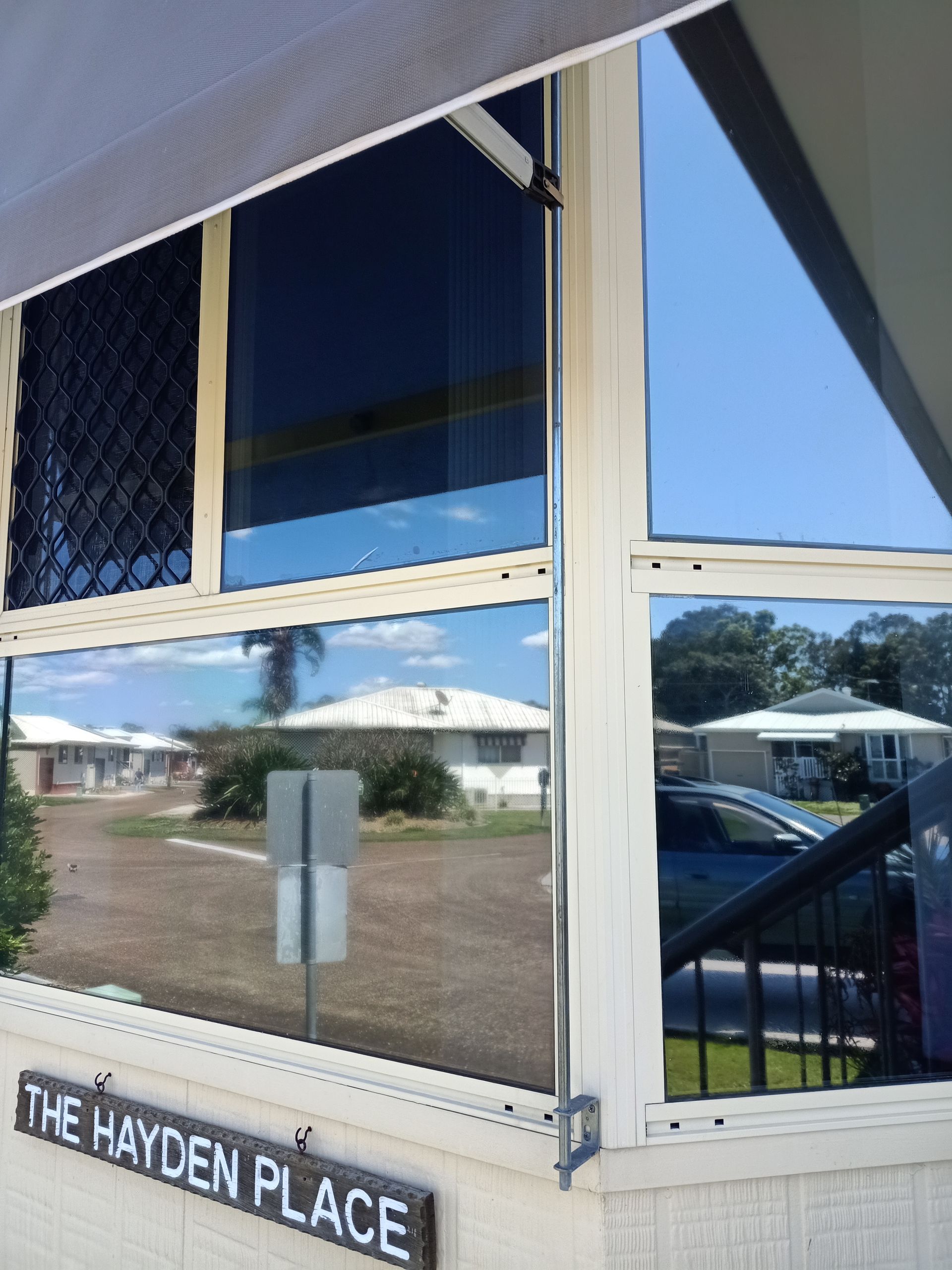 View through tinted windows showing a street, houses, and the sky. A sign reads 