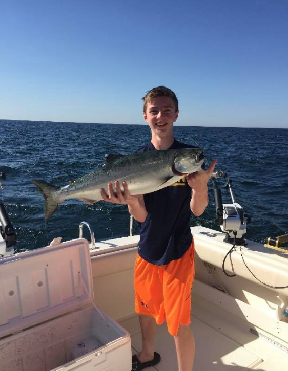 A young man is holding a large fish on a boat.
