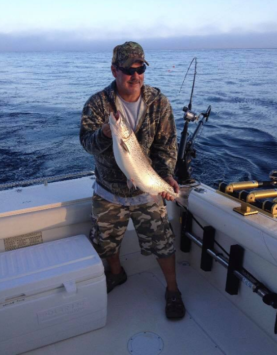 A man is standing on a boat holding a large fish.