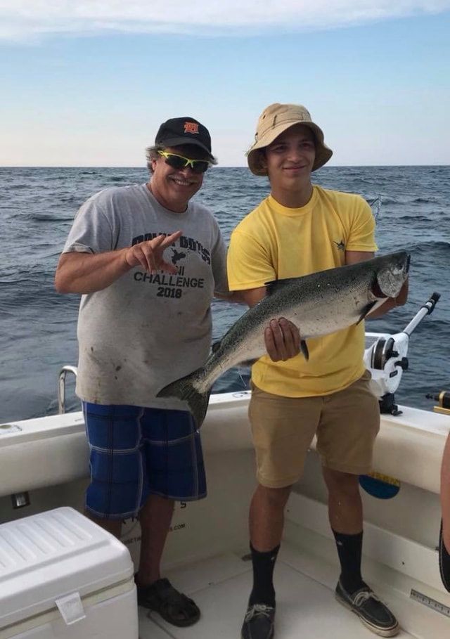 Two men are standing on a boat holding a large fish.