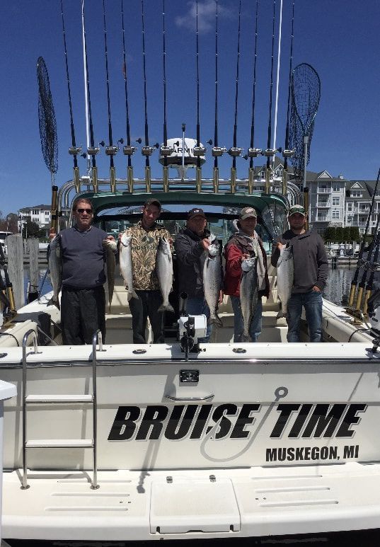 A group of men are standing on the back of a boat holding fish.