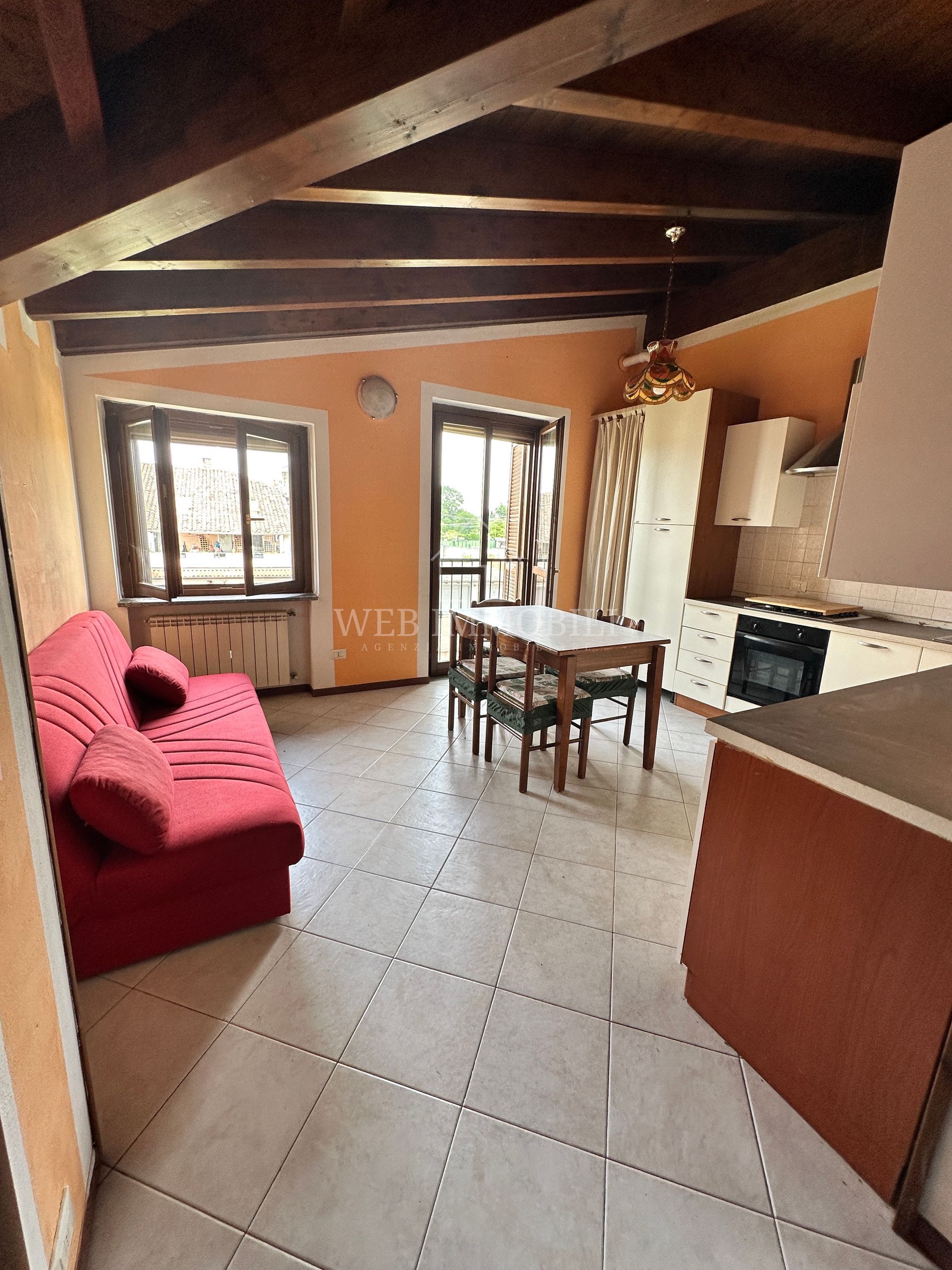 Divano rosso, tavolo da pranzo e cucina in una zona giorno con travi in ​​legno a vista.