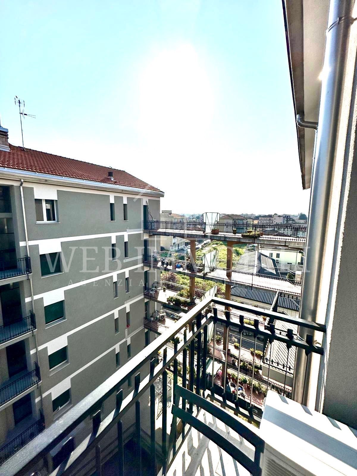 Vista dal balcone sul paesaggio urbano con edifici e cielo soleggiato.