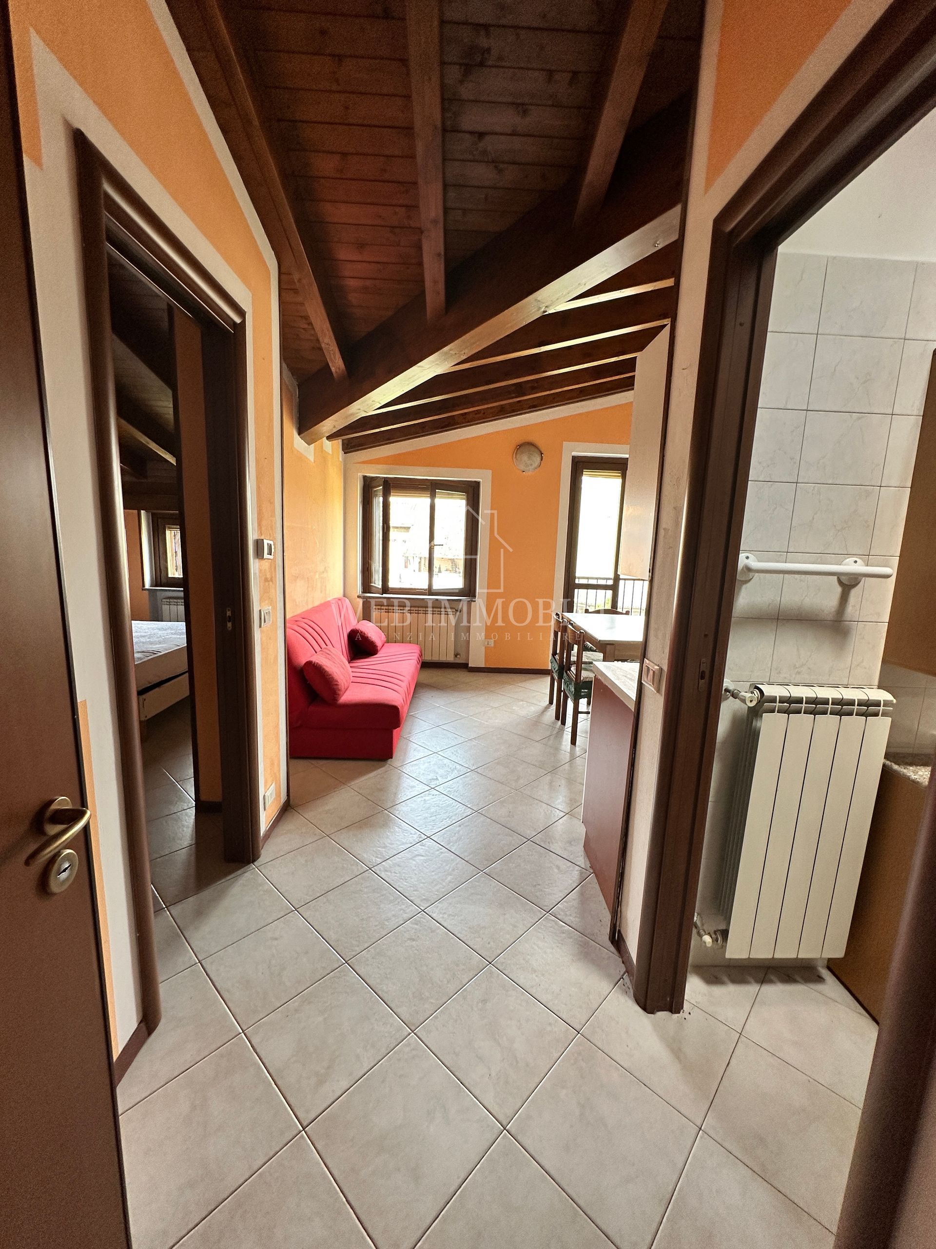 Corridoio stretto con porte che danno sulle stanze, soffitto in legno a vista, pareti arancioni e divano rosso.